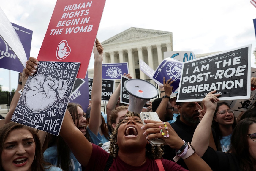 Anti-abortion demonstrators celebrate and cheer holding signs like "I am the post-Roe generation".