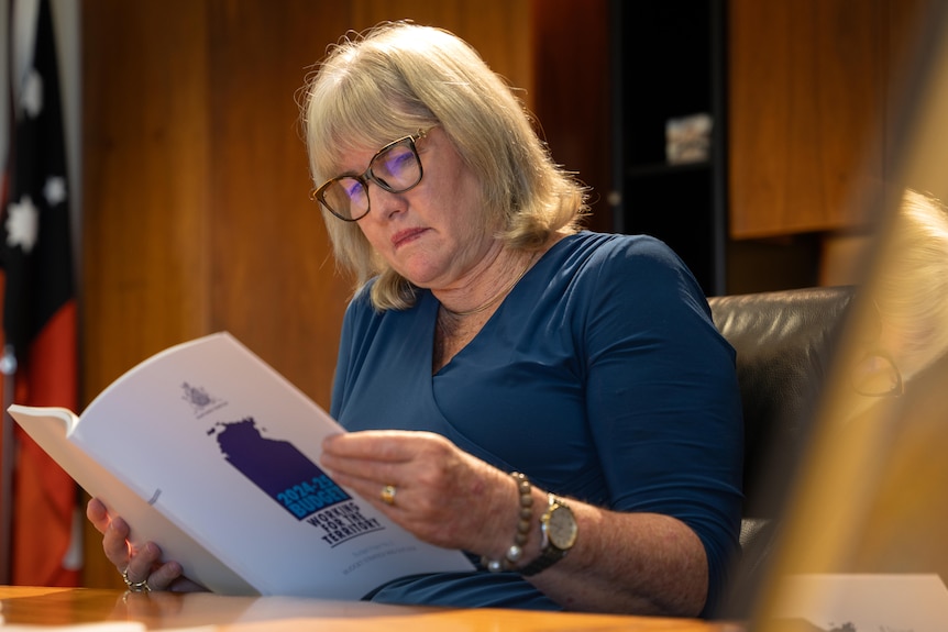 A woman with short blonde hair reads the NT 2024-25 budget papers.