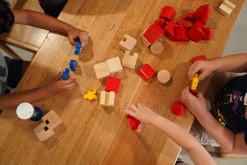 Three children play with blocks at a table in a day care centre.