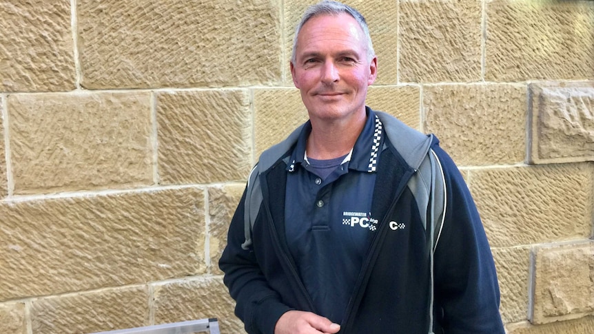 A man looks at the camera, sandstone background