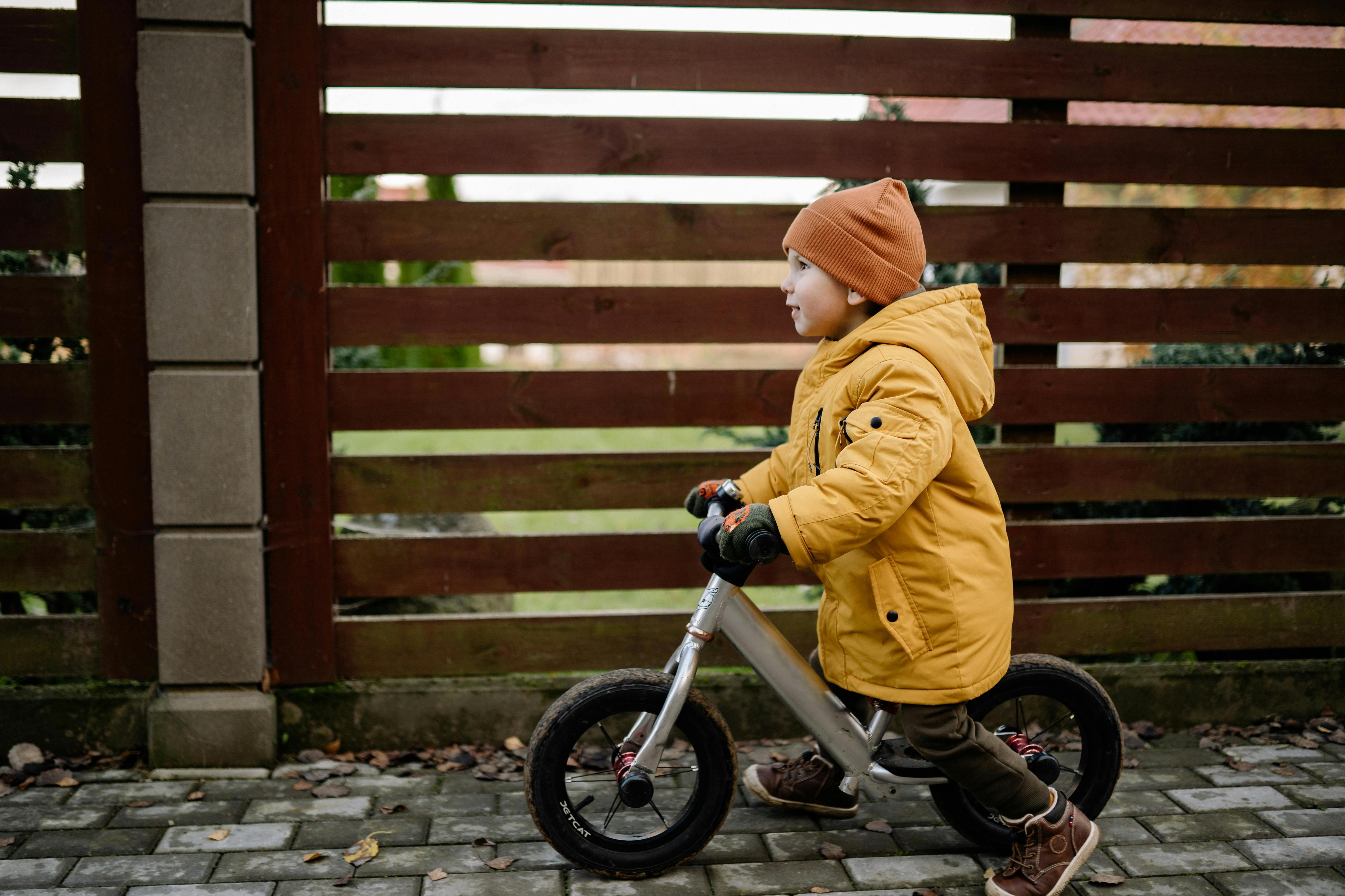 toddler on bike wearing yellow raincoat and orange beanie