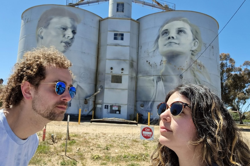 Two people in the foreground peer inward, mimicking the faces on the silo behind 