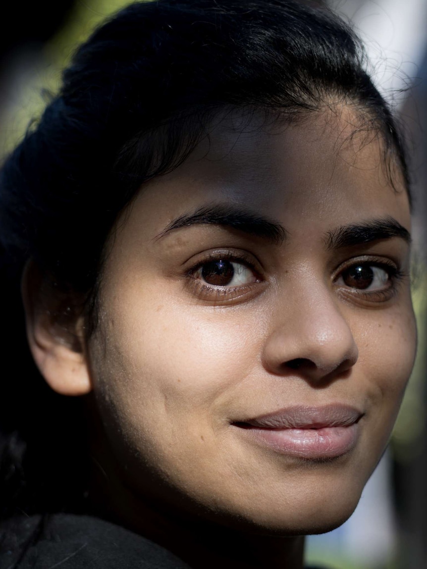 A young Indian woman looks forward, her face partially lit by the sun.