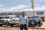Man standing in front of car dealership.