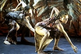 Three painted up female dancers perform on stage in front of textured backdrop.