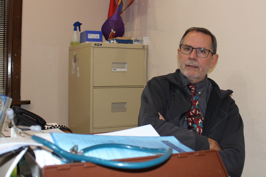 A doctor sits at his desk and a stethoscope is in the foreground.