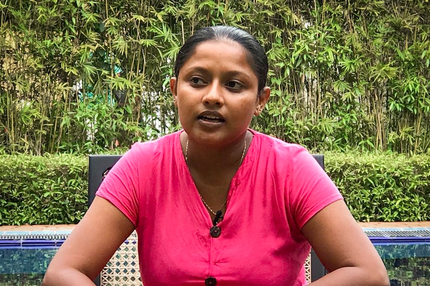 A young Sri Lankan woman in a pink top sits in front of a bamboo grove