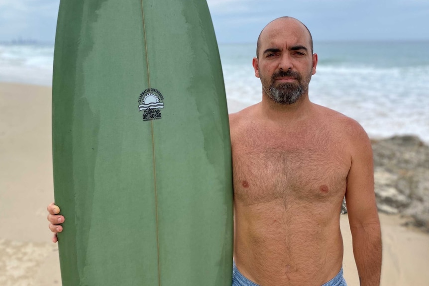 Surfer stands holding his board at the beach.