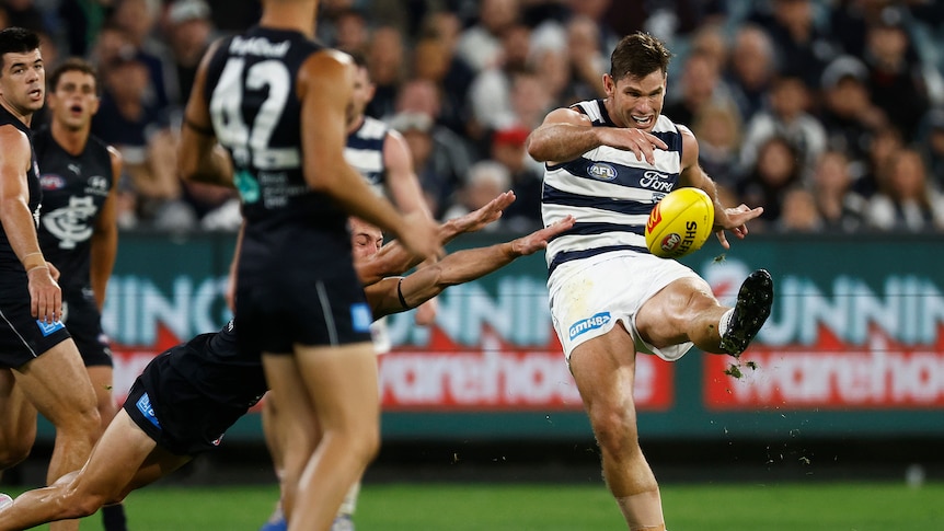 A Geelong player looks down as he tries to snap a shot at goal as Carlton players try to smother the kick.