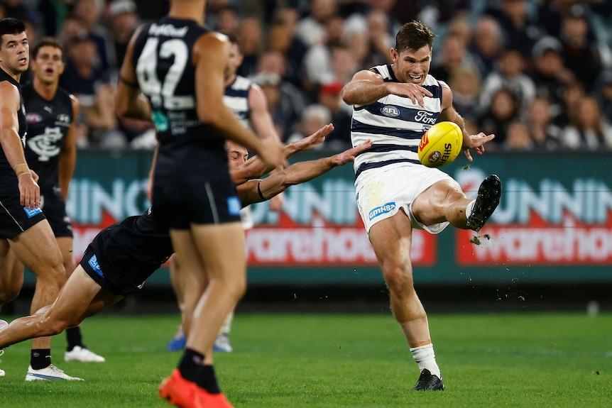 A Geelong player looks down as he tries to snap a shot at goal as Carlton players try to smother the kick.