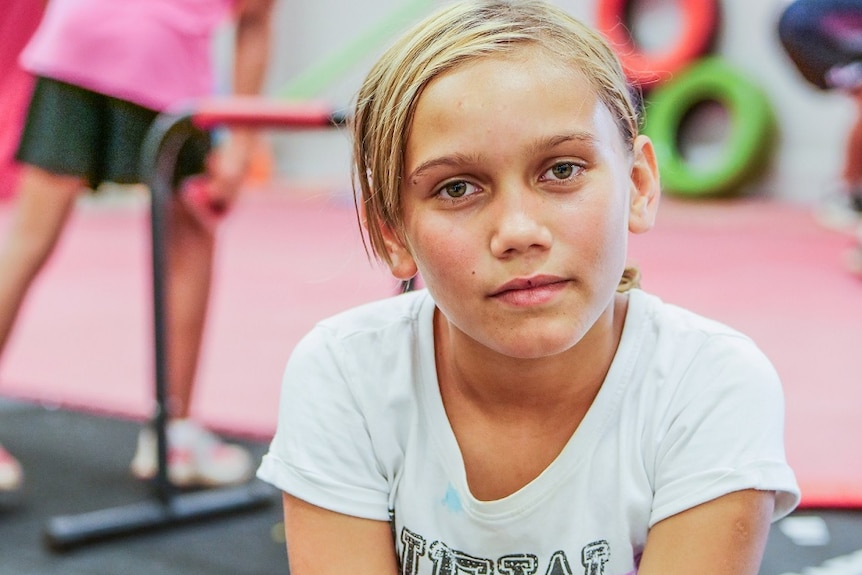 An Aboriginal girl with blonde hair, sitting, looking gently at the camera.