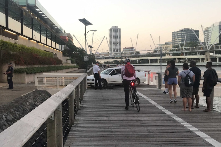 Police and security guards attempt to remove a car from a boardwalk along the Brisbane River.