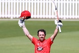 Travis Head holds his hands up in the air while holding his bat and his cricket helmet
