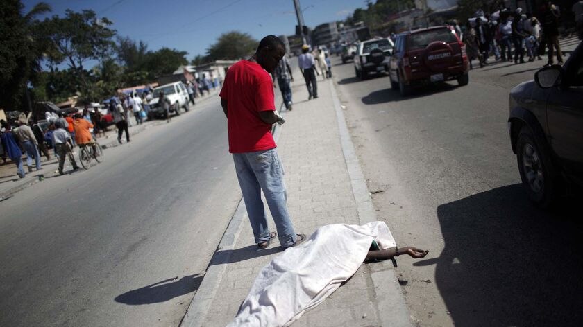 A resident walks past a body lying on a road in Port-au-Prince