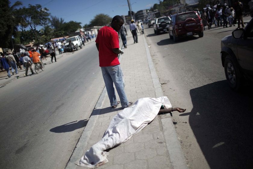 A resident walks past a body lying on a road in Port-au-Prince