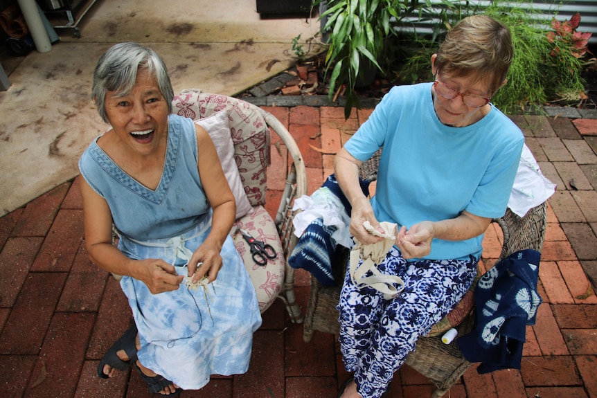 Two ladies sitting outside stitching fabric.