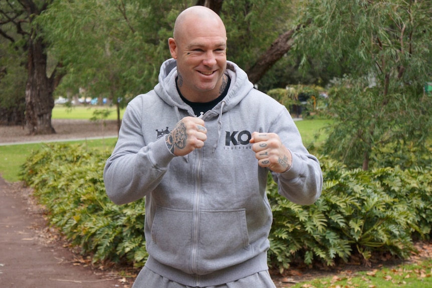 Lucas Browne strikes a boxing pose wearing a grey tracksuit standing in a park.