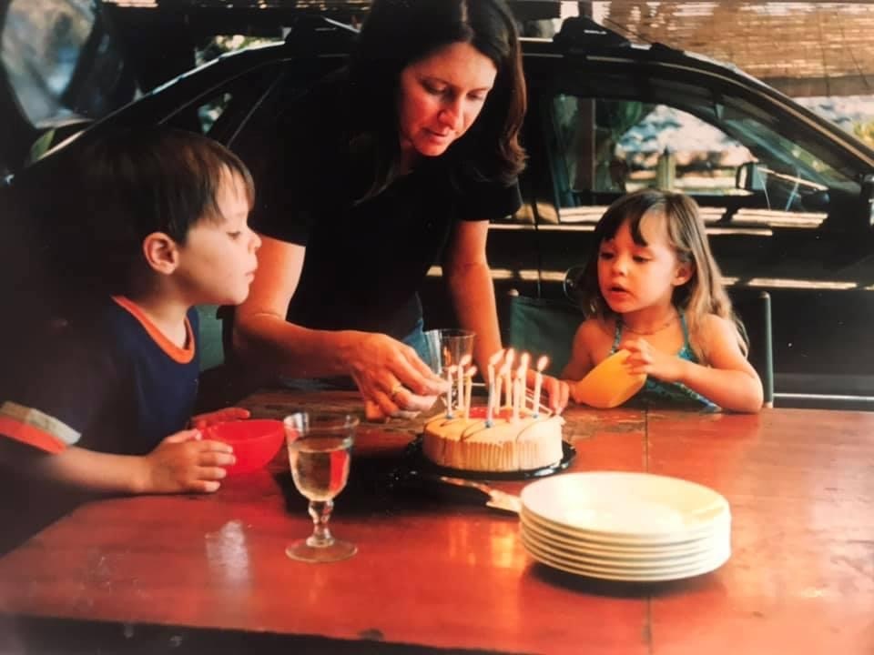 Una mujer enciende velas en una tarta de cumpleaños para dos niños