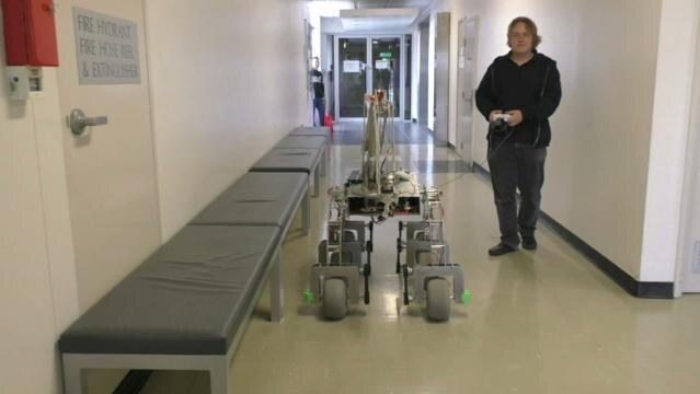 Man leads robot through corridor with a wired controller