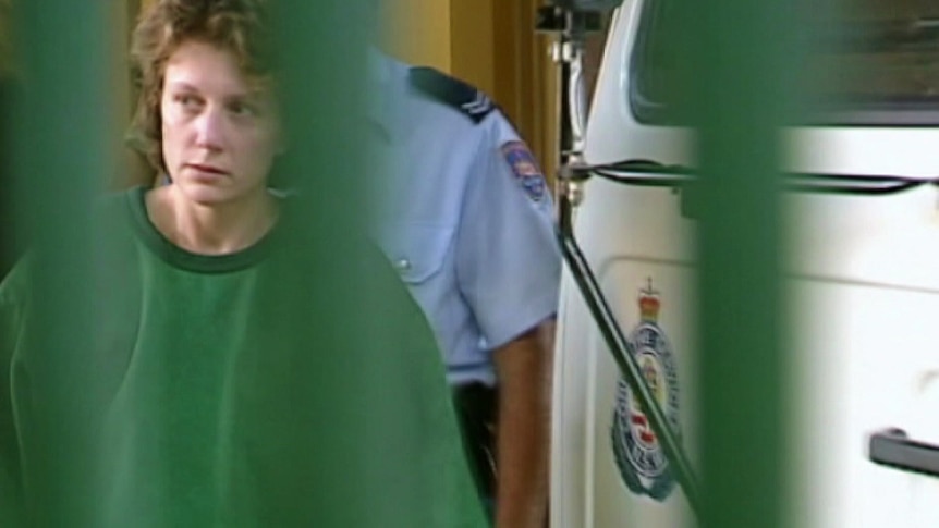 a woman wearing prison clothing walking behind a police van