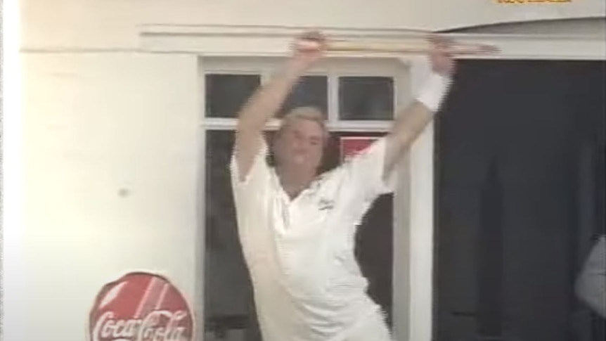 A screengrab from a YouTube video of Shane Warne dancing with a stump above his head.
