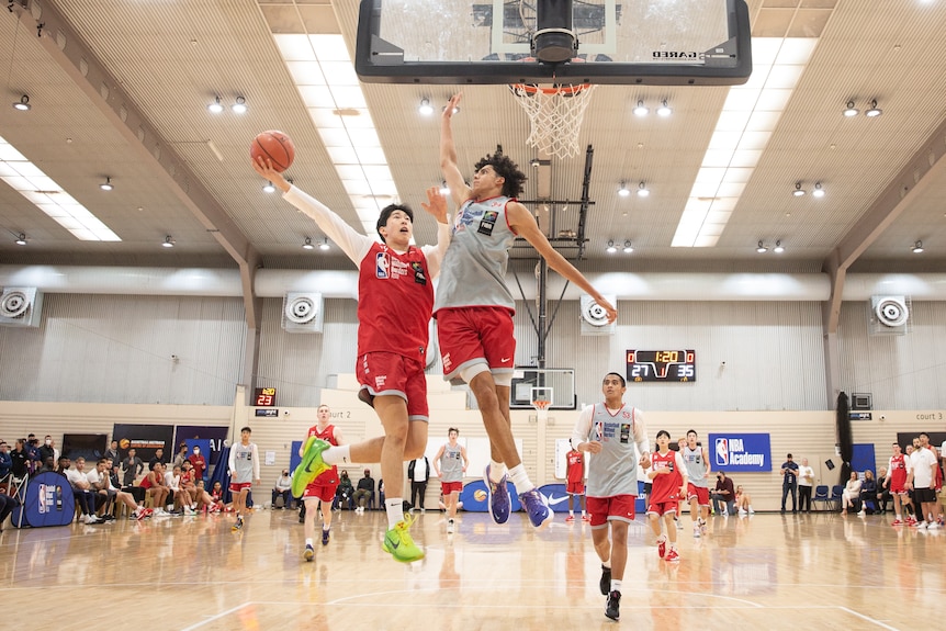 Two basketball players leap high as one tries to slam the ball into the hoop.