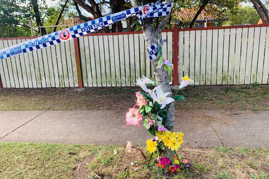Floral tributes and police tape around a tree outside a house where a 24-year-old woman's body was found at Crestmead.