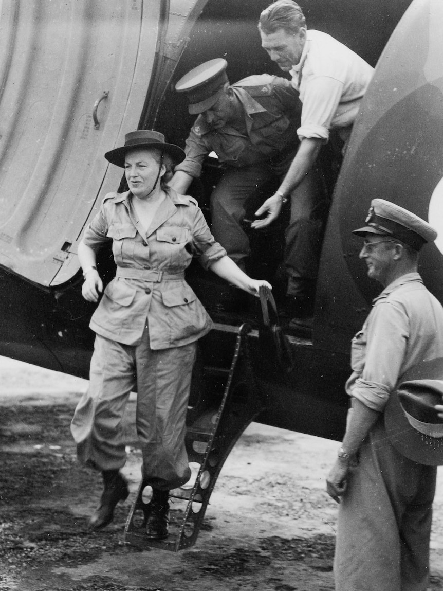 Historic monochrome image of a woman in army uniform being helped from a military aeroplane