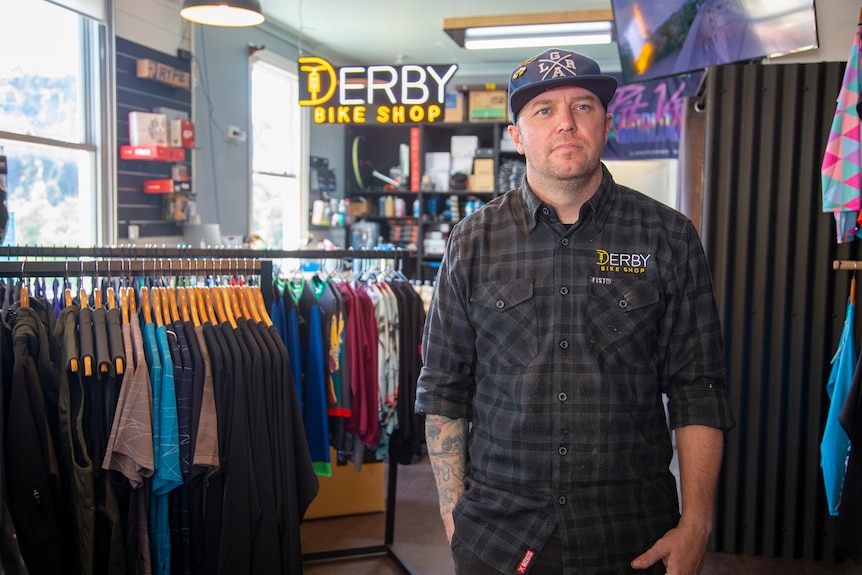 A man standing in a store, in front of racks of clothes.