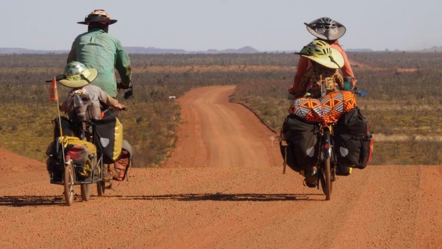 Two adults and two children ride tandem bikes along a desert road.