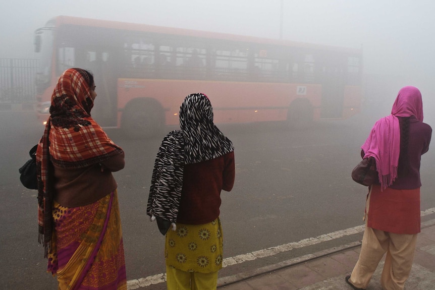 Indian commuters wait for a bus early on a polluted morning in New Delhi on January 31, 2013.