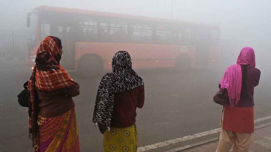 Indian commuters wait for a bus early on a polluted morning in New Delhi on January 31, 2013.