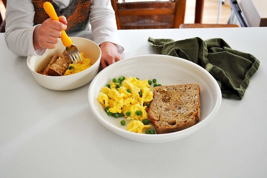 Two servings of scrambled eggs with peas and toast served in bowls.