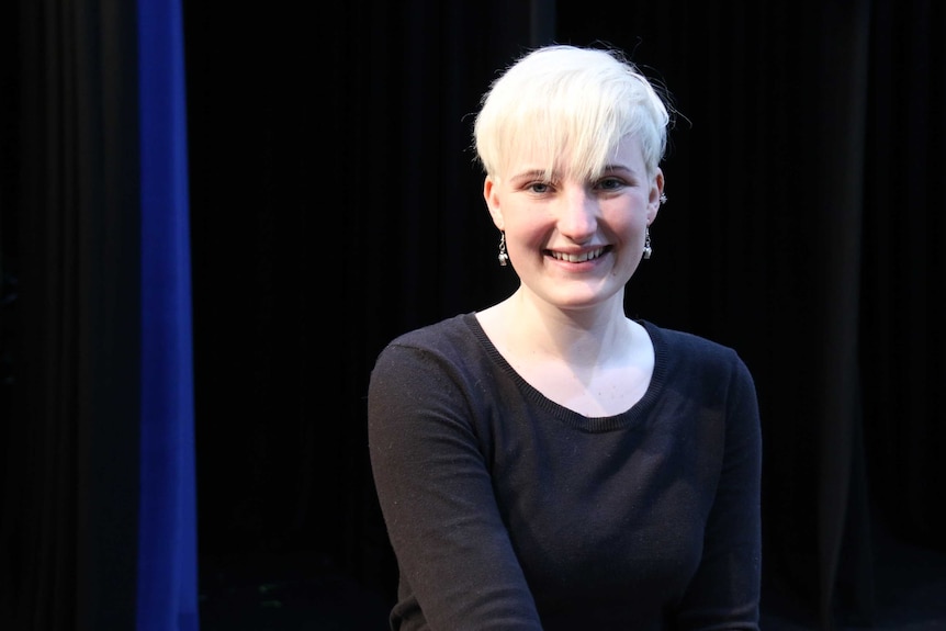 A girl with cropped blonde hair smiles at the camera.