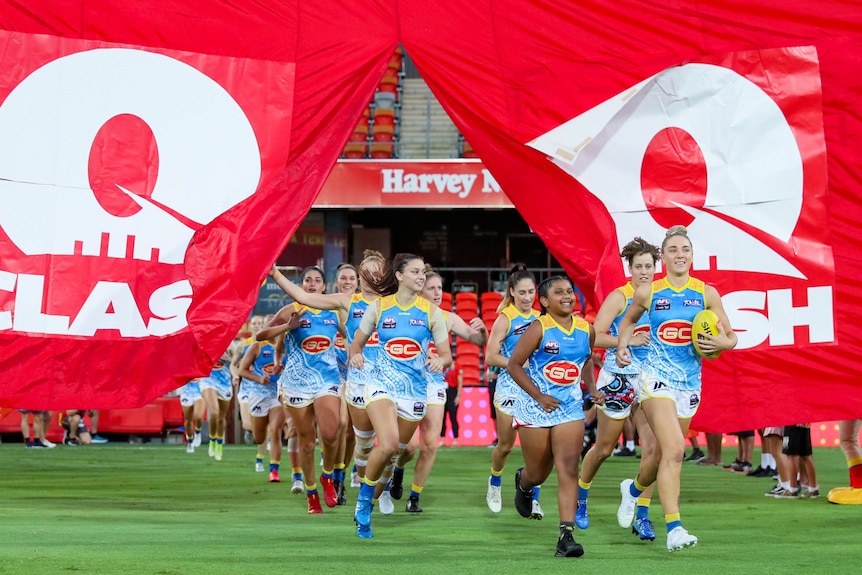 The Gold Coast Suns AFLW side runs through a Q Clash banner