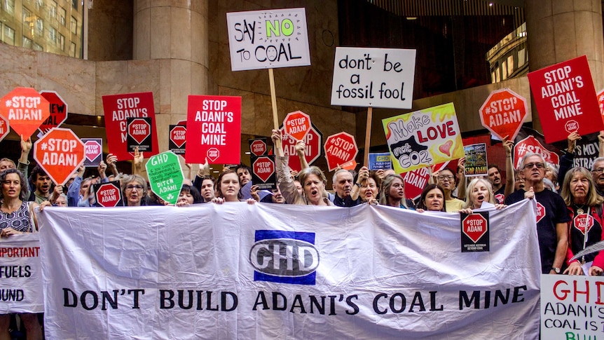 Group of people hold signs of different colours protesting Adani and GHD outside a large city building