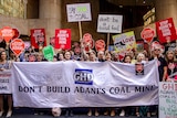Group of people hold signs of different colours protesting Adani and GHD outside a large city building