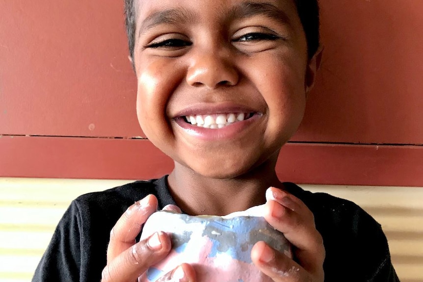 Child smiling with a piece of hand-painted pottery.