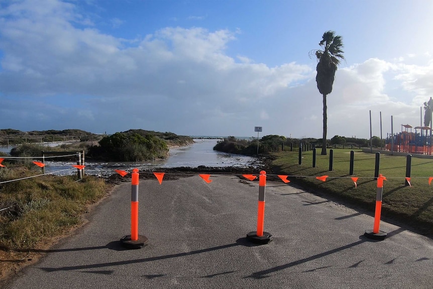 Orange flags mark off an inundated coastal footpath next to a playground.