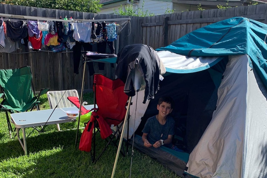 A picture of a tent set up with a child sitting in it. The tent is next to a washing line, in a suburban backyard.