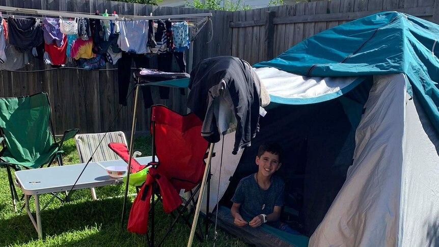 A picture of a tent set up with a child sitting in it. The tent is next to a washing line, in a suburban backyard.