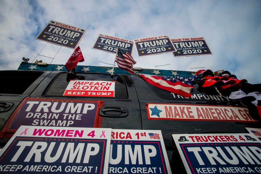 A car is covered with US flags and posters supporting Donald Trump