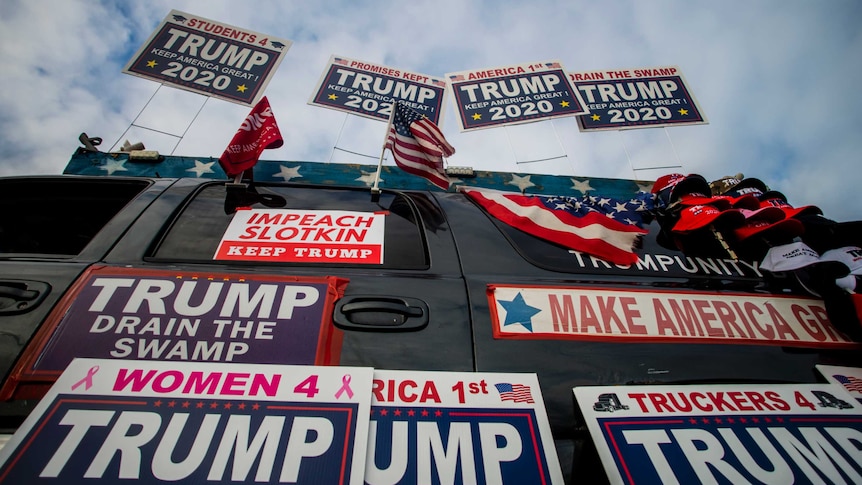 A car is covered with US flags and posters supporting Donald Trump