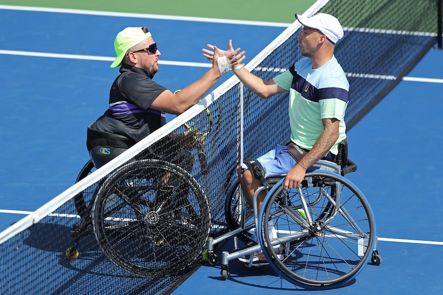 Two wheelchair tennis players meet and shake hands at the net after the men's quad singles final at the US Open. 