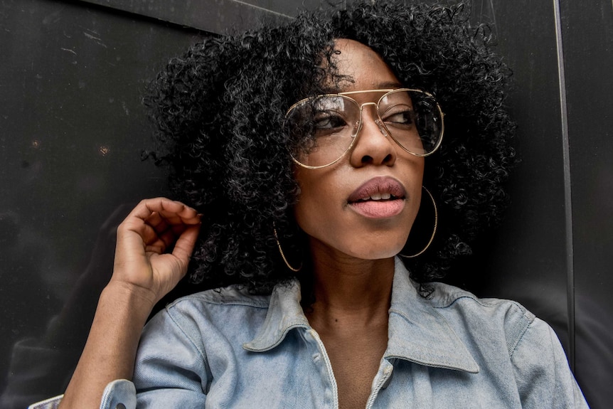 Woman with black curly hair wearing large aviators style glasses with clear lenses
