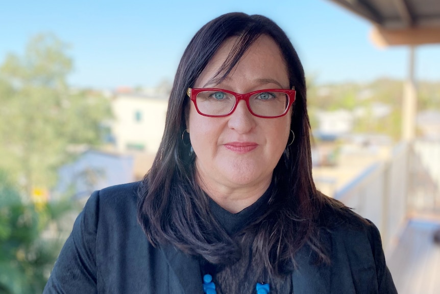 A woman wearing red glasses and a navy jacket and top.