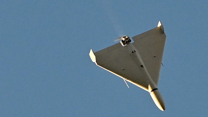 A white drone flies in blue skies.