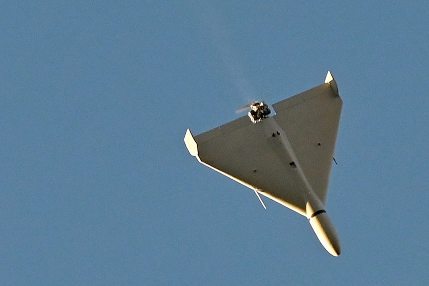 A white drone flies in blue skies.