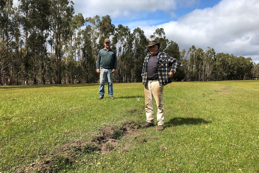Two men stand either side of a crack in a paddock, caused by an earthquake