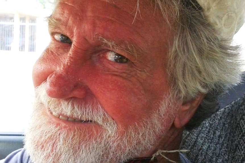 A bearded man smiling as he turns his head from the front seat of a car